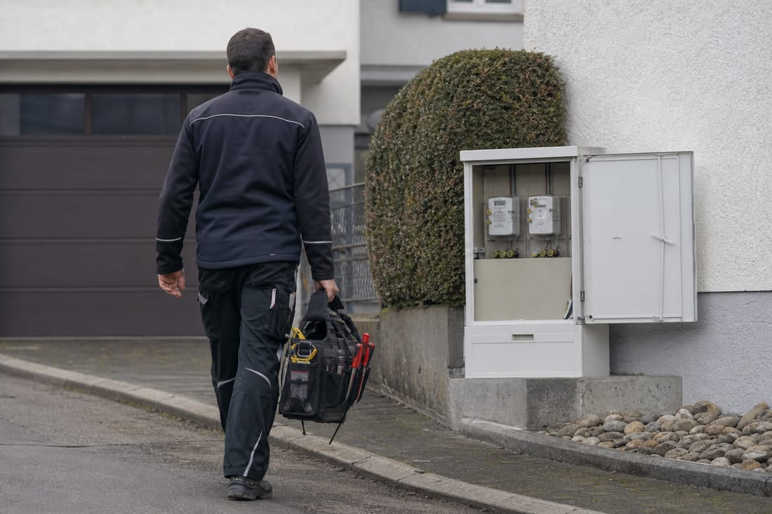 Beispiel: Elektriker von hinten mit Werkzeugtasche vor einem Hausanschluss
