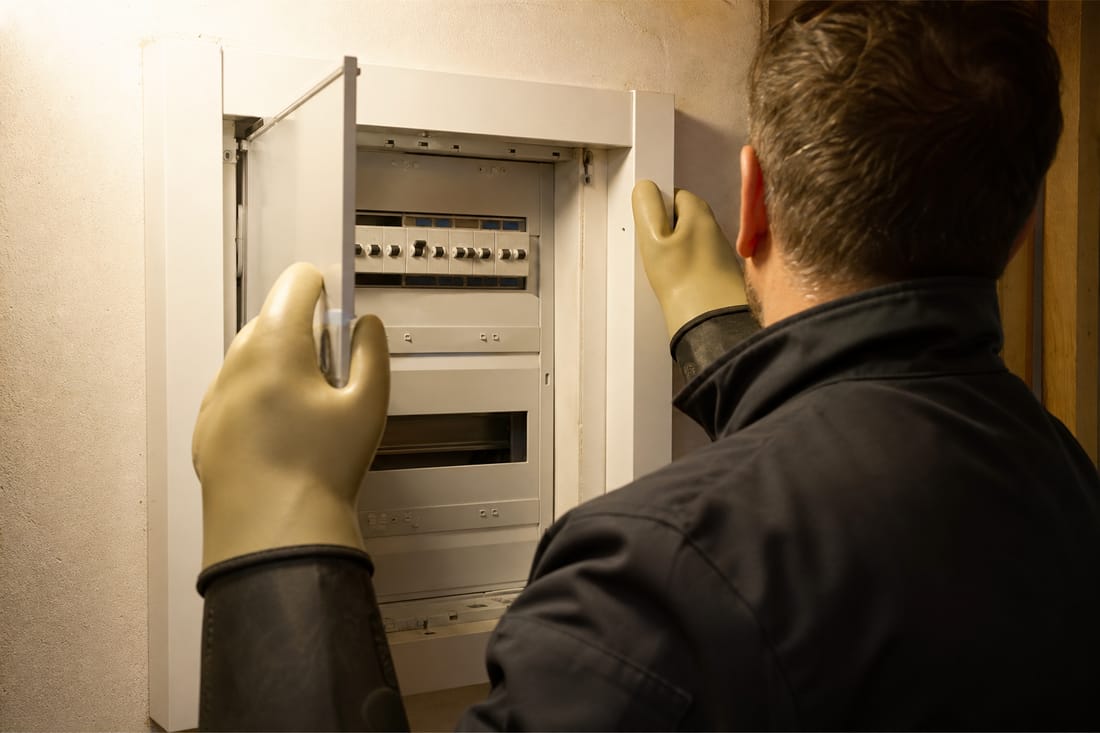 Beispiel: Elektriker von hinten öffnet mit Handschuhen einen Sicherungskasten